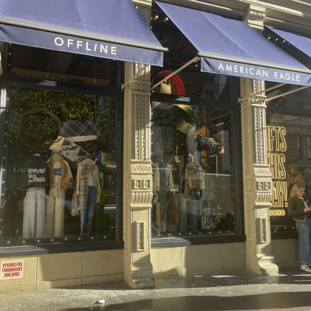 Blue awnings with American Eagle and Offline written on them extend over a sidewalk in the sun